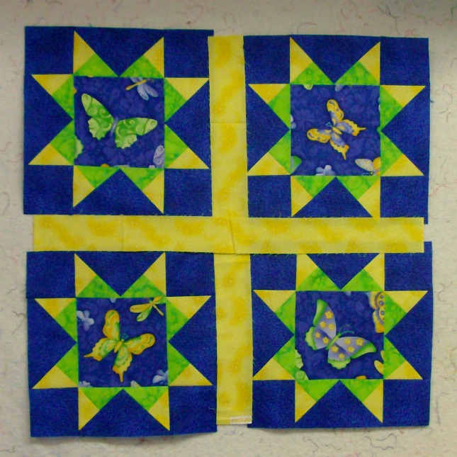 Four quilt blocks together of the Arm Star Quilt Block outlined with a yellow boarder.